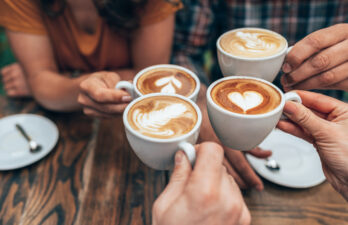 People hands holding cups of cappuccino. Friends drinking coffee together. Hands holding modern looking cups of cappuccino. Tasty and good looking coffee.